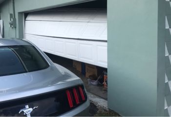 White sectional garage door visibly off track and partially tilted inside a Fort Worth home garage.