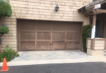 Old, weathered wooden garage door with peeling paint on a Dallas home before replacement.