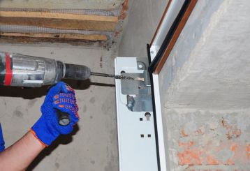 Close-up of a technician in blue gloves using a power drill to secure a metal garage door track to the wall during a new garage door installation in Cedar Hill, TX.
