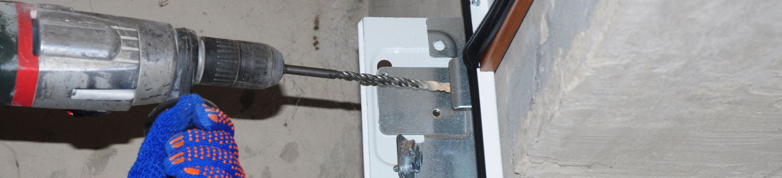 Close-up of a technician in blue gloves using a power drill to secure a metal garage door track to the wall during a new garage door installation in Cedar Hill, TX.