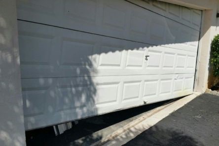 Damaged white garage door misaligned and off its lower track section – Cedar Hill project